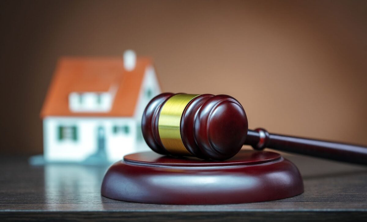 Gavel in the foreground and toy house blurred in the background.